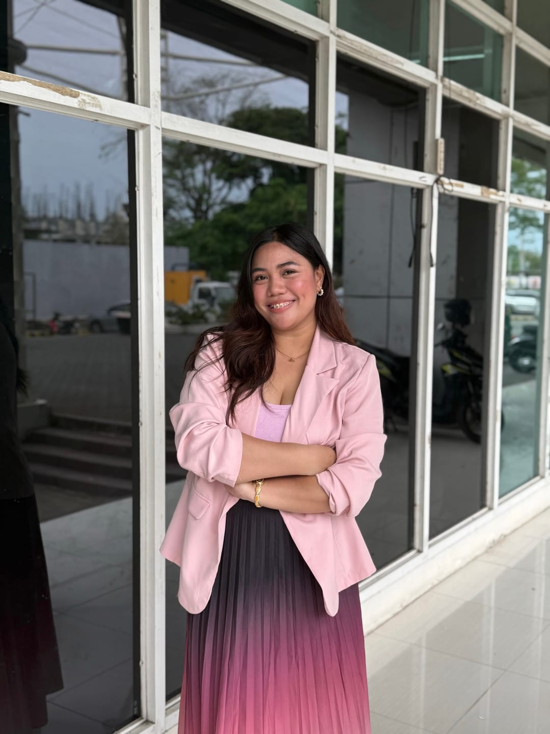 Aliyha standing with arms crossed in a pink blazer and pleated skirt